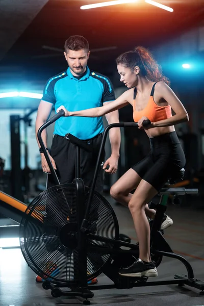 Mujer tiene entrenamiento y entrenamiento en bicicleta estática con entrenador personal en el gimnasio — Foto de Stock