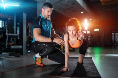 Spor salonunda kişisel antrenörle dörtlü egzersiz yapan genç bir kadın.