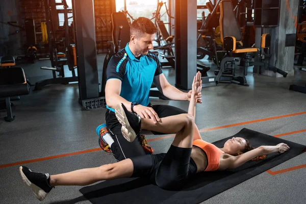 Genç bir kadın spor salonunda kişisel antrenörüyle böcek egzersizi yapıyor.