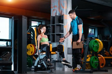 Spor salonunda antrenörle bacak açma egzersizi yapan genç bir kadın.