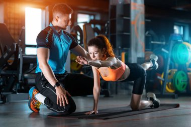 Spor salonunda kişisel antrenörle dörtlü egzersiz yapan genç bir kadın.