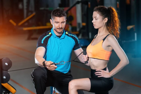 Jonge vrouw oefenen enkele arm rij knielen met personal trainer man in de sportschool — Stockfoto