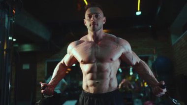 Gövdesi mükemmel vücut geliştiren sporcu spor salonunda kablo çapraz egzersizi yapıyor.