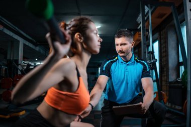 Genç bayan spor yapıyor ve spor salonunda kişisel antrenörle halter çalışıyor.
