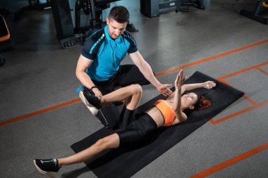 Genç bir kadın spor salonunda kişisel antrenörüyle böcek egzersizi yapıyor.