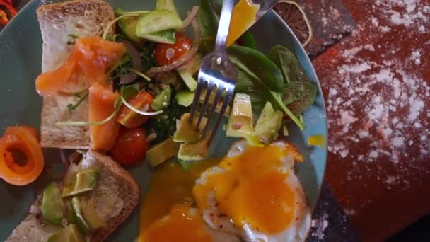 Человек завтракает с жареными яйцами, хлебом, авокадо, красной рыбой лосося — стоковое видео