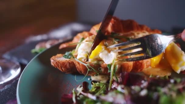 İnsan kruvasan sandviçi yer yeşil salata, haşlanmış yumurta ve pastırma ile kahvaltı yapar. — Stok video