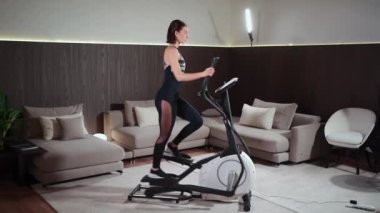 Kadın spor salonunda ya da apartmanda eliptik yörünge makinesinde koşuyor.