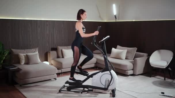 Žena běžící na eliptickém orbitreku ve fitness tělocvičně nebo apartmánu — Stock video