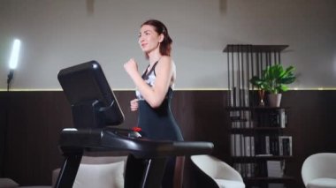 Genç fitness kadınının evde kardiyo çalışması ve koşu bandında koşması var.