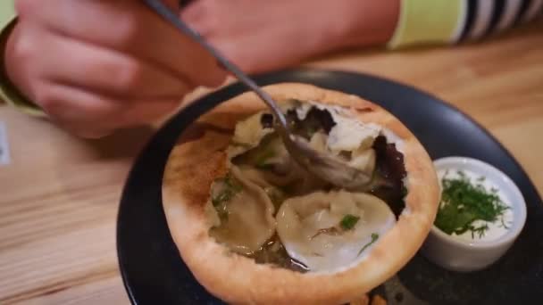 Mão com colher comer sopa com khinkali e salsa verde em tigela de massa comestível — Vídeo de Stock