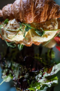 Taze kruvasan sandviçi, yeşil salata, haşlanmış yumurta ve pastırmalı kahvaltı.