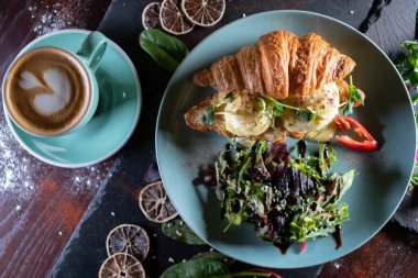 Kruvasan sandviçi, yeşil salata, haşlanmış yumurta, pastırma ve kahve.
