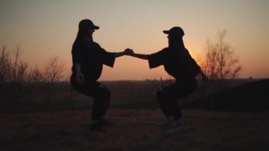 İki bayan sporcu spor yapıyor ve gün batımında açık havada egzersiz yapıyor.