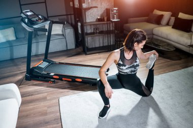 Neşeli kadın evdeki koşu bandında esniyor ve kardiyo antrenmanına hazırlanıyor.