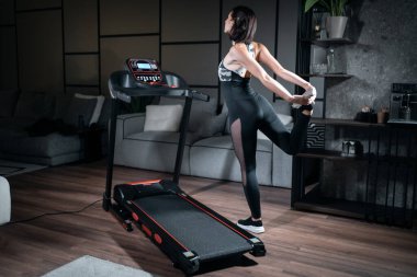 Neşeli kadın evdeki koşu bandında esniyor ve kardiyo antrenmanına hazırlanıyor.