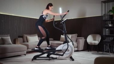 Kadın spor salonunda ya da apartmanda eliptik yörünge makinesinde koşuyor.