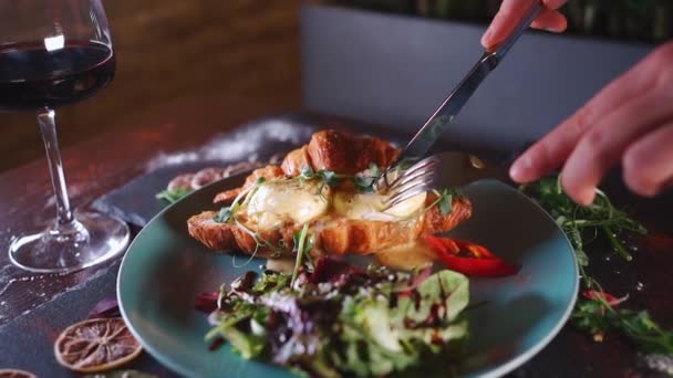 Persoon eet croissant sandwich ontbijt met groene salade, gepocheerde eieren, spek — Stockvideo