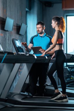Güzel bir bayan antrenörle spor salonunda koşuyor.