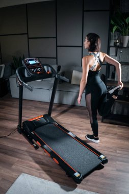 Güzel bir kadın esneyip koşu bandında antrenmana hazırlanıyor.