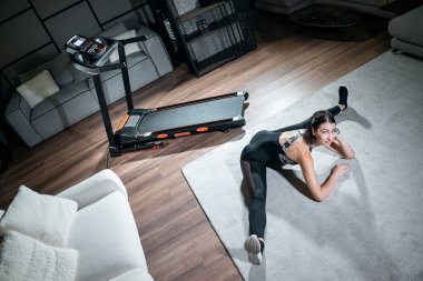 Güzel bir kadın esneyip koşu bandında antrenmana hazırlanıyor.