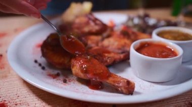 closeup of hand with spoon pouring ketchup on grilled chicken tapaka on table