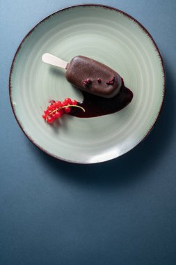 Çubuklu çikolatalı dondurma ve siyah arka planda kırmızı frenk üzümü ile süslenmiş meyve.