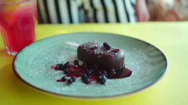 Lokantada çikolata jöleli ve meyveli çubuklu tatlı cheesecake dondurması süsleyen biri.