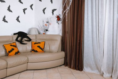 Cadılar Bayramı için dekore edilmiş oturma odasının içinde turuncu kağıt örümcekleri ya da duvarda yarasalar var. Cadılar Bayramı için tasarlanmış Cadılar Bayramı kanepede turuncu yastıklar var..