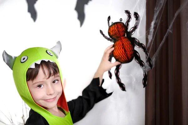 Happy little boy in monster costume touch Halloween decorations orange paper spider on a cobweb.Happy childhood. Decoration and party concept. Halloween postcard. Traditional festival of autumn.