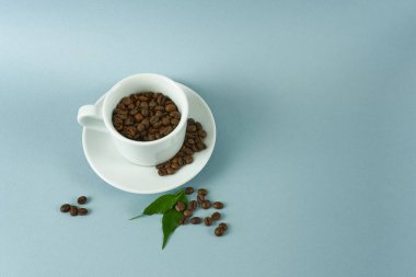 Mavi arka planda kahve çekirdekleri ile dolu beyaz fincan ve çay tabağı.