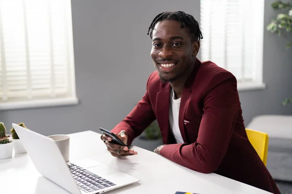 Kestane rengi ceketli patron iş adamı. Amerikalı, Afrikalı adam elinde telefonla koltukta oturuyor. Karlı bir gülümsemeyle gülümsüyor, görevlerini yapıyor..