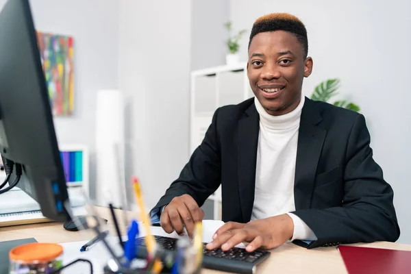 Ofis hukuk firmasında çalışan gülümseyen adam bilgisayarın önünde oturmuş verileri sisteme giren elektronik belgelerin doğruluğunu kontrol ediyor klavyede parmaklarını tıkırdatıyor.