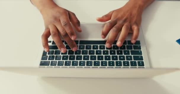 Primer plano de latop plateado de pie sobre un escritorio blanco, hombre de piel oscura trabajando en él, manos negras jóvenes, tecleando el texto en el teclado, tocando los dedos en la computadora. — Vídeos de Stock