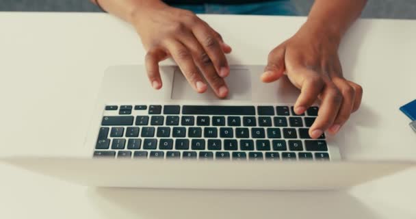 Primer plano de latop plateado de pie sobre un escritorio blanco, hombre de piel oscura trabajando en él, manos jóvenes, tecleando texto en el teclado, tocando los dedos en la computadora. — Vídeo de stock
