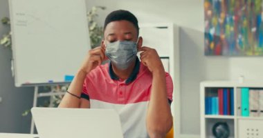 Yüzünde koruyucu maske olan koyu tenli genç bir çocuk iddialı bir projede çalışıyor. Bir ofis çalışanı kameraya bakıyor ve maskeyi gülücüklerden çıkarıyor..