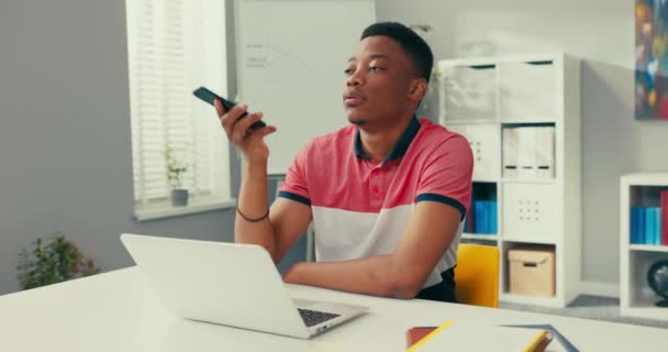 Ein Mitarbeiter einer Telemarketing-Agentur sitzt an einem Schreibtisch vor einem Laptop, wählt eine Nummer zu einem Kunden, telefoniert, stellt sich vor, lädt den Anrufer zu einem Treffen im Unternehmen ein. — Stockvideo