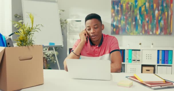 O conselheiro do cliente senta-se na mesa da empresa na frente da tela do laptop, fala no smartphone, atende o chamador, entra em dados no sistema, interrompe a chamada, desconecta na linha telefônica. — Vídeo de Stock