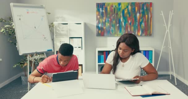 Un bel employé à la peau foncée vêtu d'un costume marron se tient dans un bureau à côté d'un tableau blanc, dessine un graphique, explique les relations, organise une séance de formation, une conférence. — Video