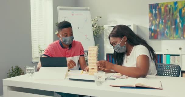 Ruptura en la oficina del trabajo, dos jóvenes internos están construyendo torre de bloques de madera en el escritorio, por detrás viene jefe descontento en traje granate, arruina la diversión para los empleados al aplastar el edificio. — Vídeo de stock