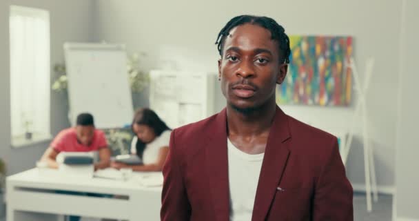 Elegant man with dreadlocks stubble, dark complexion, looks to side and into camera with brown eyes, smiles broadly showing straight white teeth wearing maroon jacket white t-shirt. — Stock Video