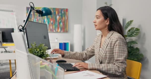 An attractive, experienced company accountant sits in office in front of a computer checking statistical data employee salary charts comparing paper diagrams with electronic ones financial analyst. — Stock Video