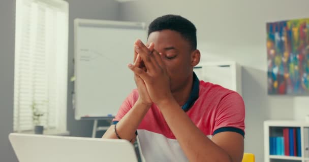 Joven chico de piel oscura se sienta desplomado frente a la computadora, apoya las manos bajo la cara, malas noticias, perder dinero, exceso de trabajo, tristeza, fatiga, angustia, estrés, decepción. — Vídeos de Stock
