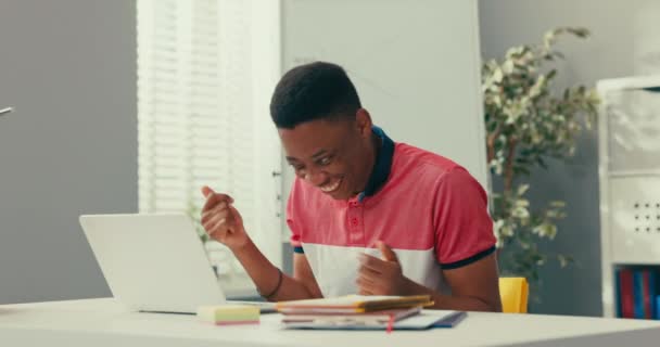 Der dunkelhäutige Junge im T-Shirt ist fertig, telefoniert zufrieden mit den verkauften Dienstleistungsprodukten und sitzt vor dem Computer, die Hände zu Fäusten geballt, blickt in die Kamera, lächelt — Stockvideo