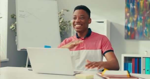 Boy with dark skin in tshirt is satisfied with sold service products, happy with the monthly profits, sitting in front of computer victory dance, hands clenched into fists looking into camera, smiling — Stock Video