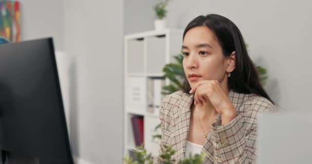 Una mujer bonita y enfocada con el pelo castaño largo usando una chaqueta a cuadros se sienta en el escritorio en la oficina frente a la pantalla de la computadora, leyendo noticias, artículos, documentos, analizando la mano de apoyo bajo la barbilla. — Vídeos de Stock