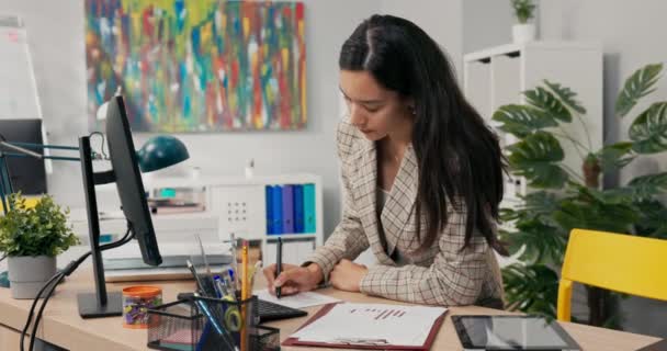 Intelligente vrouw die werkt in de financiële analyse marketing berekent bedrijfswinsten zit in kantoor vult in grafieken voert gegevens in computer markeert belangrijke dingen op documenten completeert rapporten. — Stockvideo