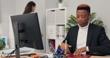 Koyu tenli ofis çalışanı masadaki bilgisayarın önünde oturup web kamerasıyla internet bağlantısı kurarak şirket meselelerini iş arkadaşlarıyla tartışarak tamamlanmış çizelge projesini açıklıyor..