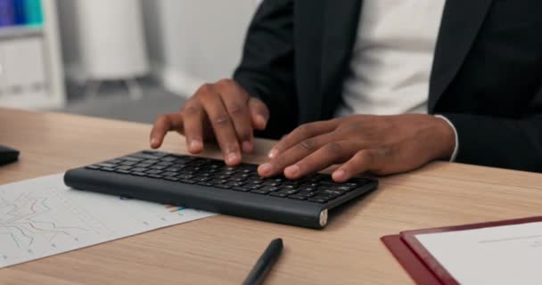 Acercamiento de un teclado negro desde una computadora de pie sobre un escritorio de madera, un hombre de piel oscura con manos jóvenes está trabajando en ello, escribiendo texto en el teclado, tocando los dedos en las teclas. — Vídeos de Stock