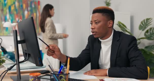 Hombre guapo de piel oscura, trabajador de oficina corporativo pasa la mañana frente a la computadora, puntos en la pantalla, cuenta, reflexiona, comprueba la corrección de los gráficos, completa los datos. — Vídeos de Stock